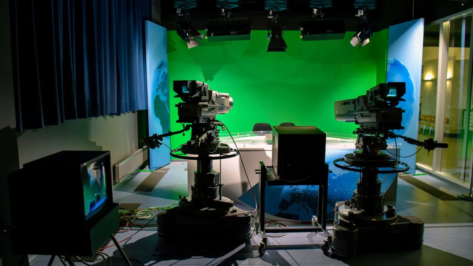 A television studio with two broadcast cameras aimed at an empty, brightly lit green screen set.